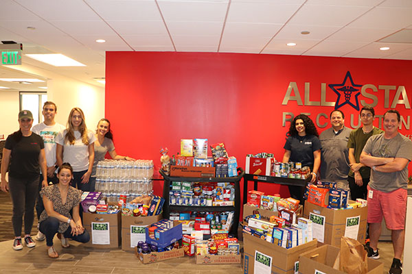 Employees standing next to food collected for food drive